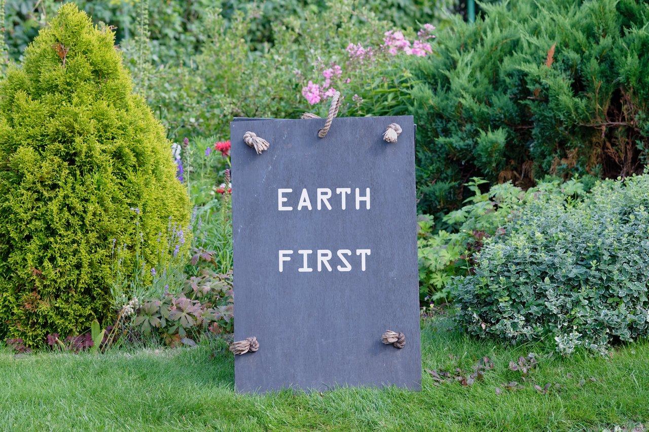 Signalisation d'événement hybride nature : panneau en ardoise dans un jardin luxuriant avec message écologique.