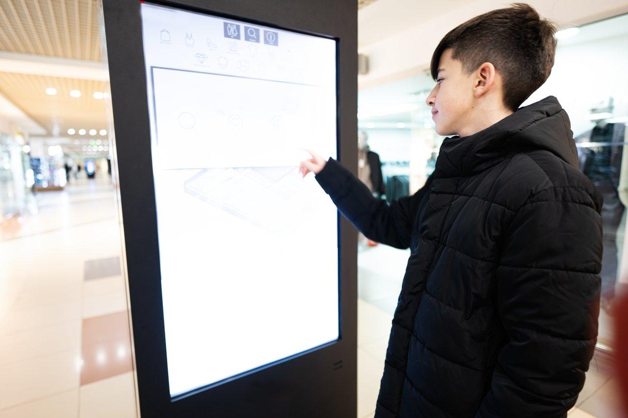 Un totem interactif numérique lumineux à hauteur d’œil attire l’attention dans une vitrine urbaine.
